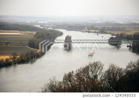 A cargo ship moving along a winding river, crossing under a steel bridge. The mix of farmland and A cargo ship moving along a winding river, crossing under a steel bridge. The mix of farmland and 124349333
