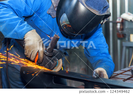 Worker in protective gear grinds metal, creating sparks in an industrial setting at metal fabrication Worker in protective gear grinds metal, creating sparks in an industrial setting at metal fabrication 124349462
