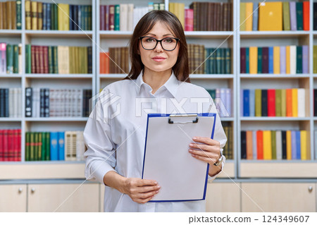 Portrait serious middle aged woman with clipboard inside library office Portrait serious middle aged woman with clipboard inside library office 124349607