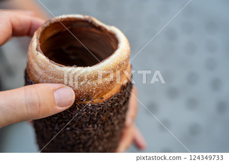 Budapest, Hungary, August 30, 2022. Close up of a Chimney cake topped with cream and chocolate pralines. Street food lifestyle. Budapest, Hungary, August 30, 2022. Close up of a Chimney cake topped with cream and chocolate pralines. Street food lifestyle. 124349733
