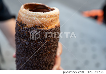 Budapest, Hungary, August 30, 2022. Close up of a Chimney cake topped with cream and chocolate pralines. Street food lifestyle. 124349736