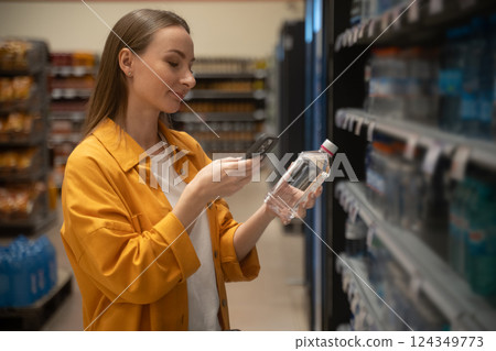 Scanning a bottle of water while shopping in a grocery store aisle with a phone 124349773