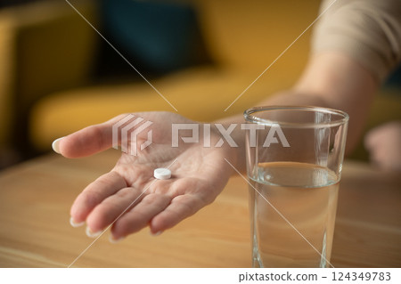 Hand shows tablet and glass of water in a home setting for health and wellness purposes Hand shows tablet and glass of water in a home setting for health and wellness purposes 124349783