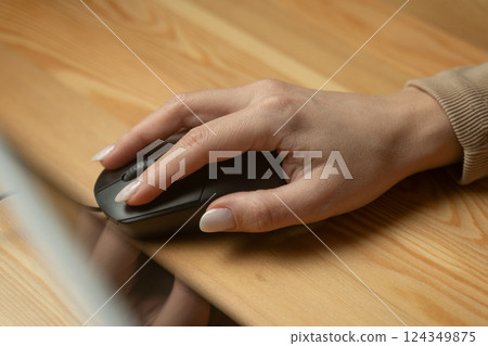 Using a computer mouse for work at a desk with a wooden surface during daytime hours Using a computer mouse for work at a desk with a wooden surface during daytime hours 124349875