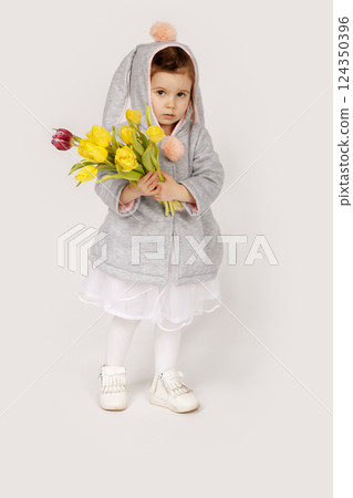 Thoughtful Toddler in Bunny Costume Holding a Bouquet of Yellow and Burgundy Tulips 124350396