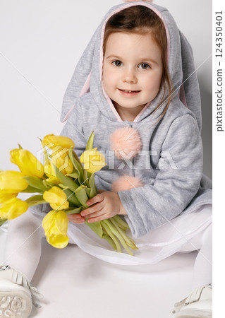 Smiling Toddler in Bunny Costume Holding Yellow Tulips on White Grey Background 124350401