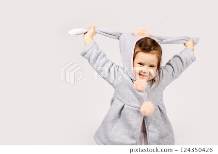 Playful Toddler in Bunny Costume Stretching Ears and Smiling on White Background 124350426