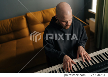 Top view of focused musician male composing music playing on synthesizer in home studio. Artist creating melodic composition, recording new song on electric piano. Concept of recording music at home. Top view of focused musician male composing music playing on synthesizer in home studio. Artist creating melodic composition, recording new song on electric piano. Concept of recording music at home. 124350731