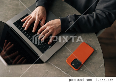 Close-up high-angle view of unrecognizable freelancer remote working from home office, developing software solutions, sitting at table by window in room. Concept of remote job, technology, people. Close-up high-angle view of unrecognizable freelancer remote working from home office, developing software solutions, sitting at table by window in room. Concept of remote job, technology, people. 124350736