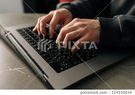 Close-up cropped shot of unrecognizable programmer male typing on laptop keyboard, immersed in software development or coding, sitting at table by window in dark room. Concept of remote job, freelance 124350834