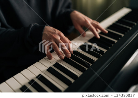 Close-up hands of unrecognizable male composer playing synthesizer in living room. Closeup of talented musician creating beautiful melodic composition using digital piano at home studio. 124350837