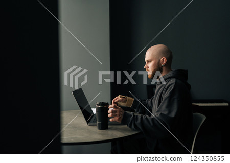 Side view of concentrated freelancer male with wrist brace working on laptop computer at home, enjoying coffee sitting in dark room. Concept of dedication and perseverance in remote work environment. Side view of concentrated freelancer male with wrist brace working on laptop computer at home, enjoying coffee sitting in dark room. Concept of dedication and perseverance in remote work environment. 124350855