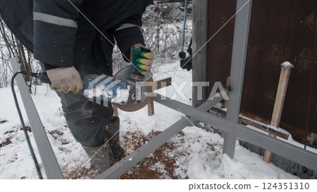 A person skillfully cutting metal with a specialized tool in a snowy environment, highlighting winter construction work A person skillfully cutting metal with a specialized tool in a snowy environment, highlighting winter construction work 124351310
