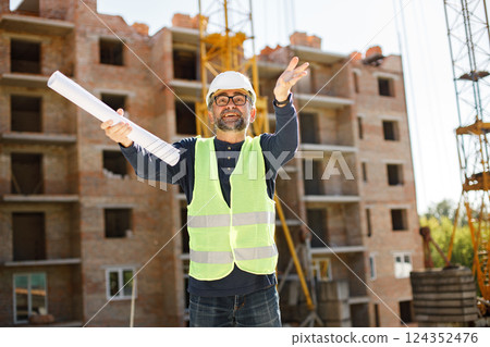 Construction site manager standing wearing safety vest. Man giving an order to workers. Construction site on a background. 124352476