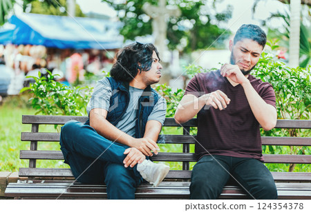 Man smoking and exhaling smoke to another person near him. Man smoking cigarette near people in public 124354378