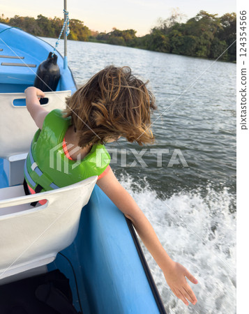Child enjoying boat ride on tranquil lake during sunny afternoon in nature 124354566