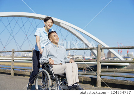 A caregiver walking a senior man in a wheelchair 124354757
