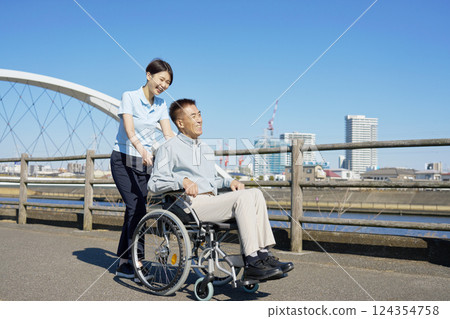 A caregiver walking a senior man in a wheelchair 124354758