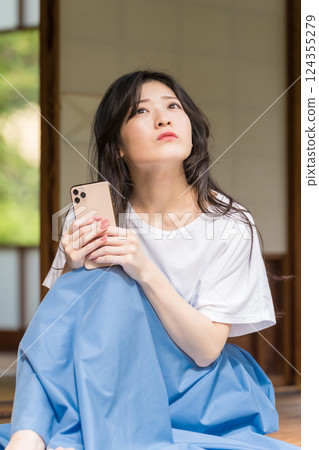 一位年輕女子手裡拿著智慧型手機思考 一位年輕女子手裡拿著智慧型手機思考 124355279