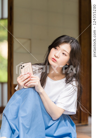 一位年輕女子手裡拿著智慧型手機思考 一位年輕女子手裡拿著智慧型手機思考 124355280