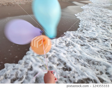 Three colorful inflatable balls on background of sea during strong winds. Person playing with multi-colored air balloons in hand on background sea waves on sandy beach of seashore. Entertainment fun Three colorful inflatable balls on background of sea during strong winds. Person playing with multi-colored air balloons in hand on background sea waves on sandy beach of seashore. Entertainment fun 124355333