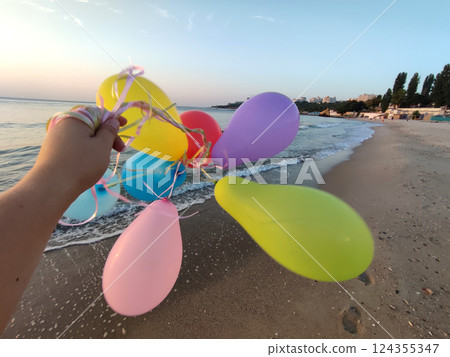 Woman playing with many colorful balloons on the sandy beach of the seashore near the sea at sunrise and sunset. Relax and have fun. Slow motion 124355347