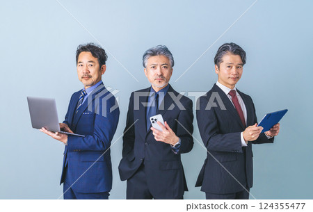 Group of middle-aged male business people holding various digital devices 124355477
