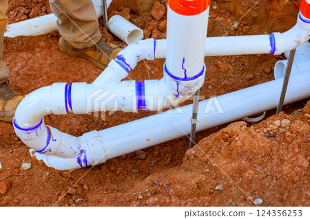 Connected pvc wastewater pipe sections in trench, ensuring alignment installation under work day Connected pvc wastewater pipe sections in trench, ensuring alignment installation under work day 124356253