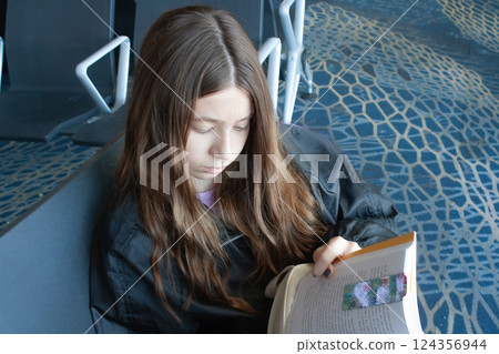 Girl reads as she waits for her plane to depart.Close-up photo 124356944