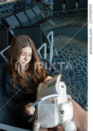 Young girl waits at the airport reading a book. 124356950