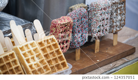 Assorted waffle and chocolate pops on sticks, arranged on a rustic wooden display 124357051