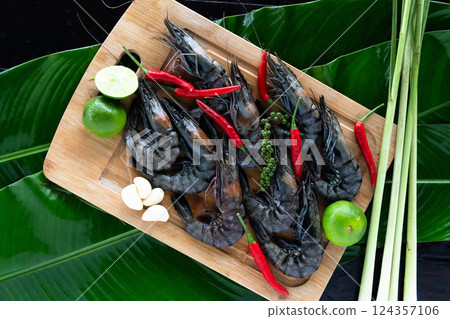 Plump tiger shrimp are artfully arranged on large banana leaves alongside vibrant green limes, garlic, and fresh chilies, showcasing the essence of Asian cuisine. 124357106