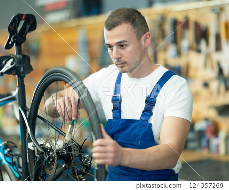 Professional male master and seller wearing uniform fixing bike, lubricating bicycle chain in sport store Professional male master and seller wearing uniform fixing bike, lubricating bicycle chain in sport store 124357269