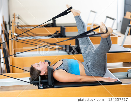 Young woman doing exercises on Pilates reformer with feet in straps 124357717