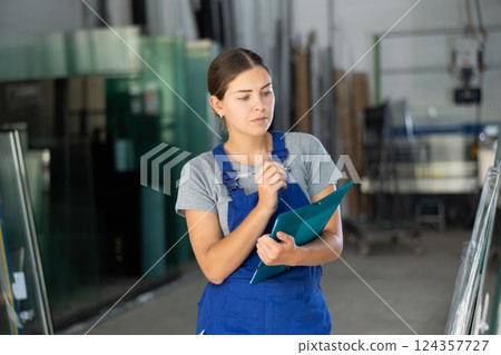 Female technician inspecting glass panels and writing notes in workshop Female technician inspecting glass panels and writing notes in workshop 124357727