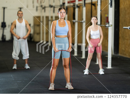 Young girl working out with other athletes with resistance band, strong biceps or abdominal muscles in gym Young girl working out with other athletes with resistance band, strong biceps or abdominal muscles in gym 124357770