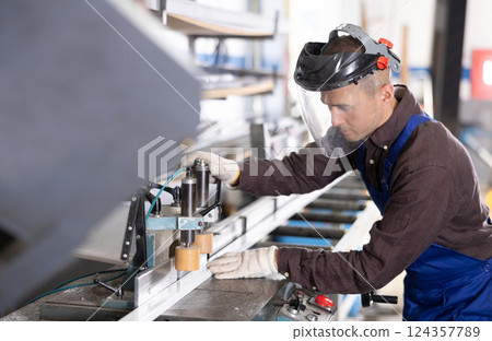 Workman cutting PVC profile on industrial machine in production workshop Workman cutting PVC profile on industrial machine in production workshop 124357789