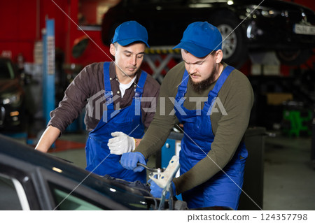 Two professional auto mechanics repairing broken car together in car service center Two professional auto mechanics repairing broken car together in car service center 124357798