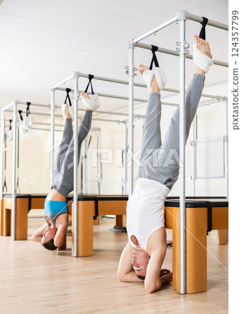 Man hanging upside down on Pilates trapeze table in fitness studio 124357799