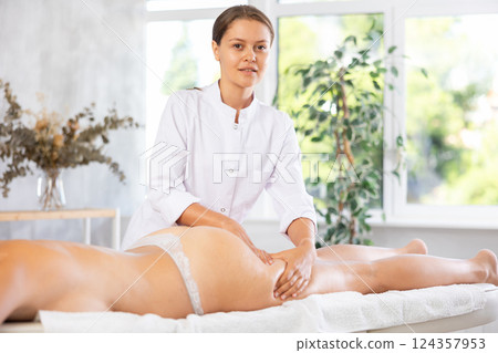 Professional young female therapist doing thigh and buttocks massage to woman Professional young female therapist doing thigh and buttocks massage to woman 124357953