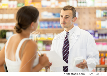 Male pharmacist consulting young girl about medicament in box Male pharmacist consulting young girl about medicament in box 124358119