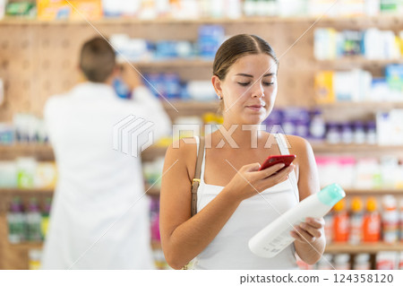 In pharmacy girl customer scans code on shampoo label, photographs packaging. In pharmacy girl customer scans code on shampoo label, photographs packaging. 124358120
