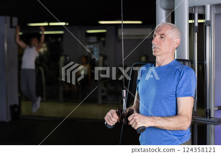 Mature man in sportswear training on rope loop simulator in gym Mature man in sportswear training on rope loop simulator in gym 124358121