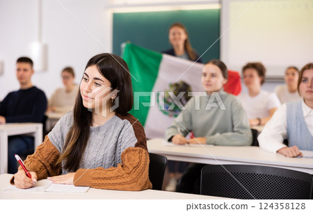 Female teacher tells her classmates about the country of Mexico, holding a flag in hands 124358128