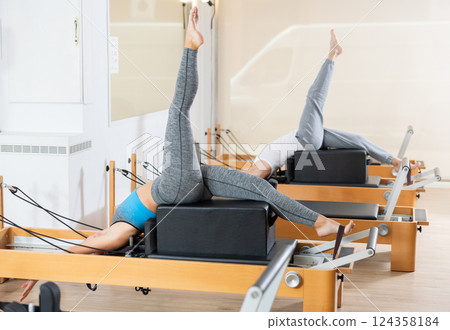 Girl doing exercises on reformer using sitting box in pilates studio Girl doing exercises on reformer using sitting box in pilates studio 124358184