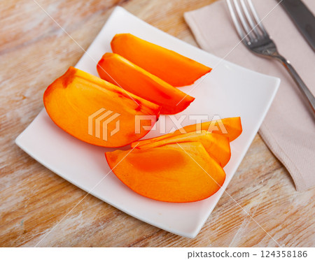 Large slices of ripe orange persimmon are served on plate. Large slices of ripe orange persimmon are served on plate. 124358186