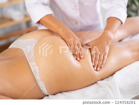 Professional therapist doing anti-cellulite thighs and buttock massage to woman Professional therapist doing anti-cellulite thighs and buttock massage to woman 124358201