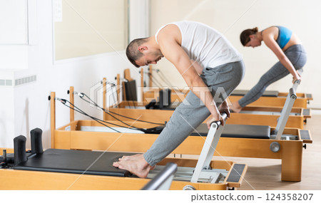 Focused man practicing exercises on Pilates reformer in studio 124358207