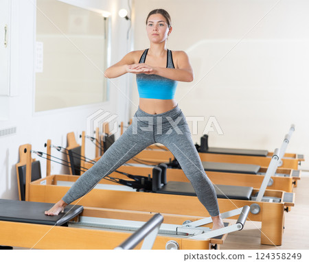 Young girl performing pilates exercises on reformer in studio 124358249