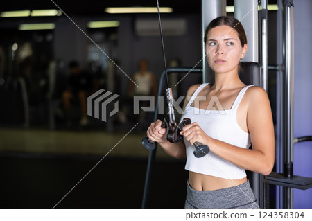 Athletic girl work out muscles of arms and shoulders on rope loop simulator in gym of fitness club 124358304